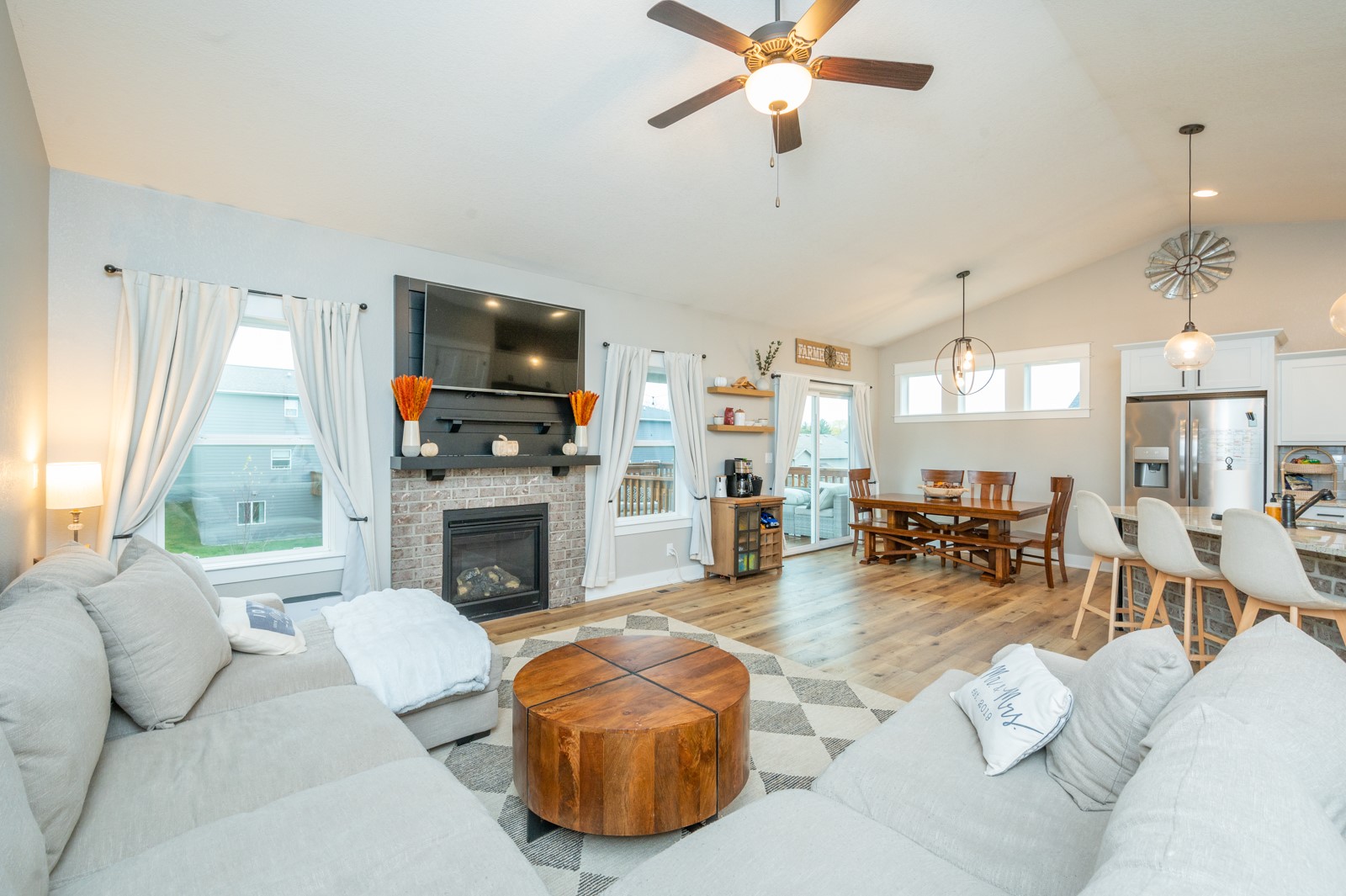 Open-plan living room with gray sectional sofas, a brick fireplace, and dining area.