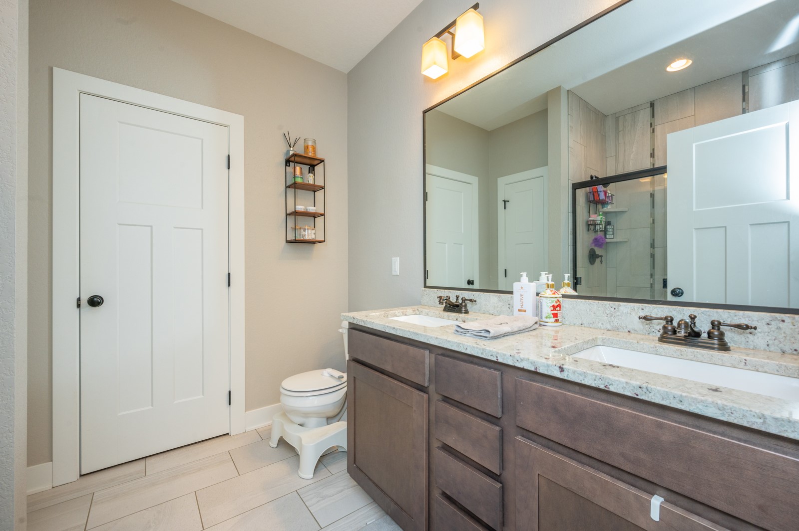 Bathroom with a double vanity, light stone countertop, and glass-enclosed tiled shower.