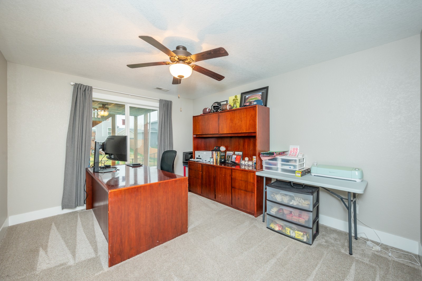 Home office with a large wooden desk, matching storage cabinets, and sliding glass doors.