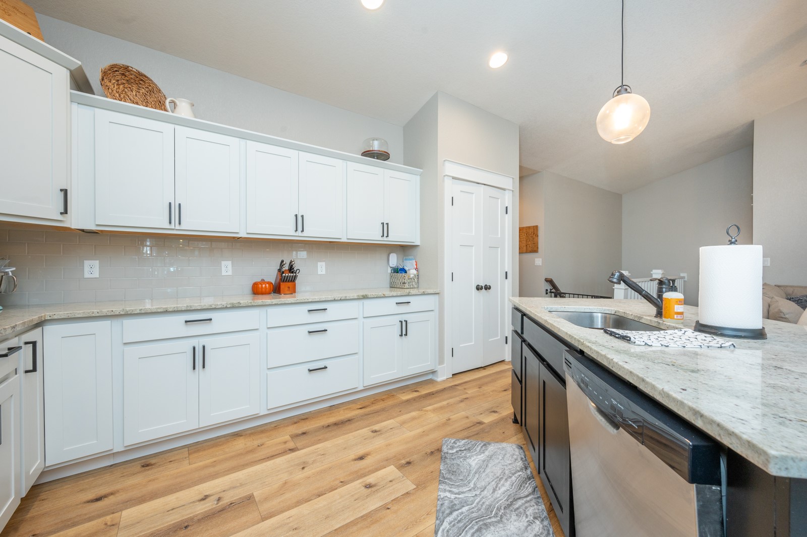 Kitchen with white shaker cabinets, a dark sink island, gray tile backsplash, and warm wood flooring.