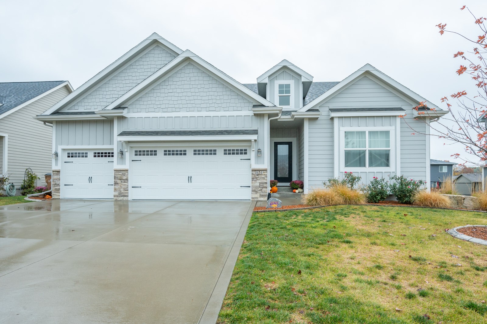 Light gray gabled home with two garage doors, stone accents, and a wet driveway.