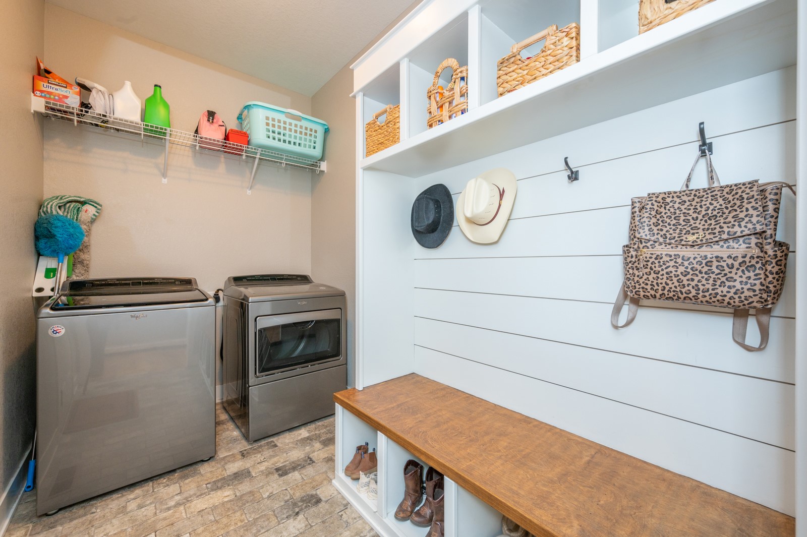 Laundry and mudroom with washer and dryer beside built-in cubbies, hooks, and a long wood-topped bench.