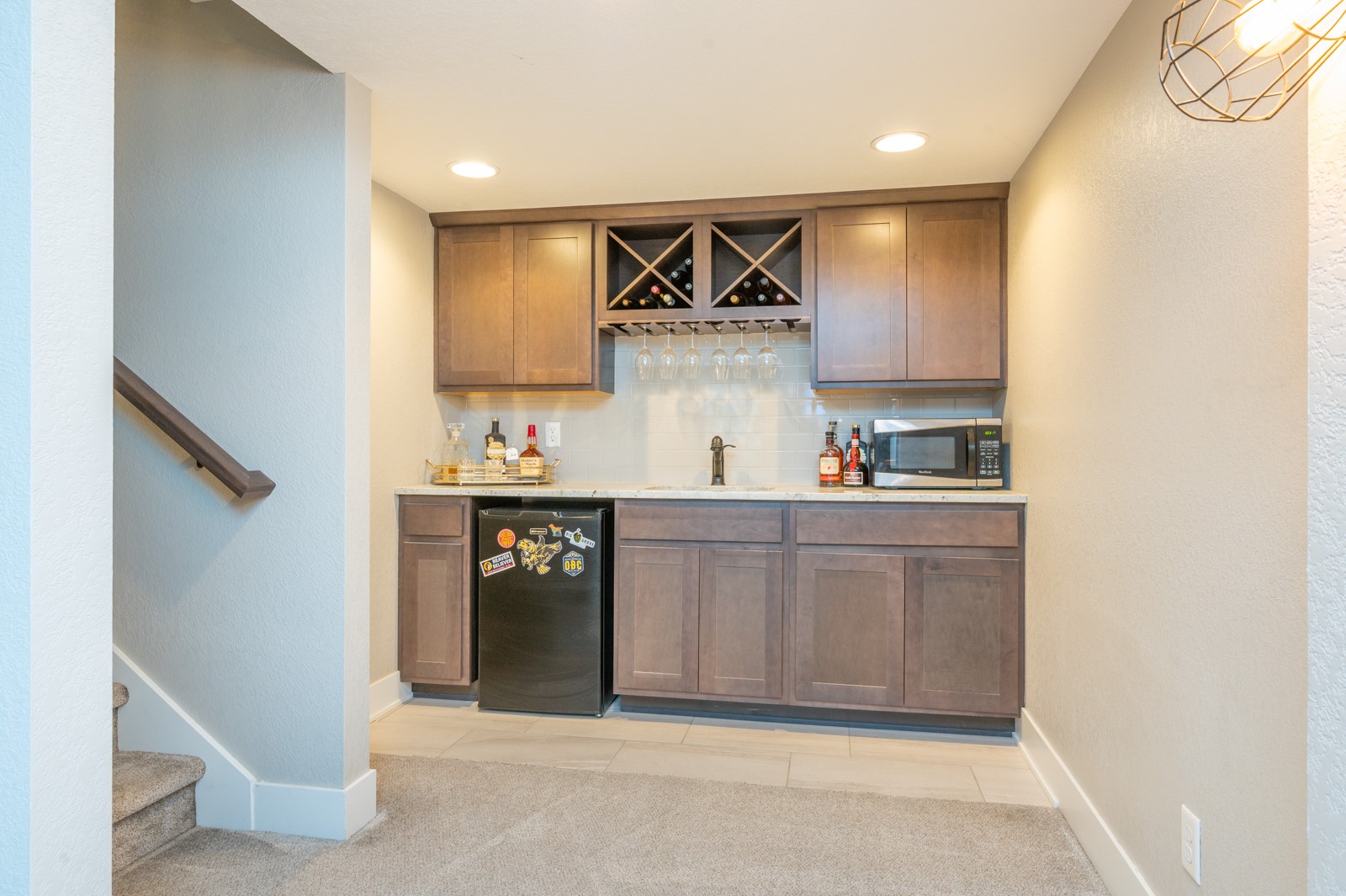 Wet bar with dark wood cabinetry, wine racks, and a beverage refrigerator beside a staircase.