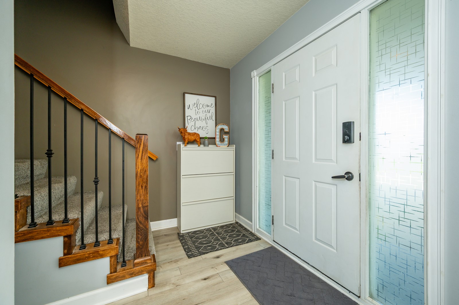 Home entryway with a white front door, patterned glass sidelights, and a wood-railed staircase.