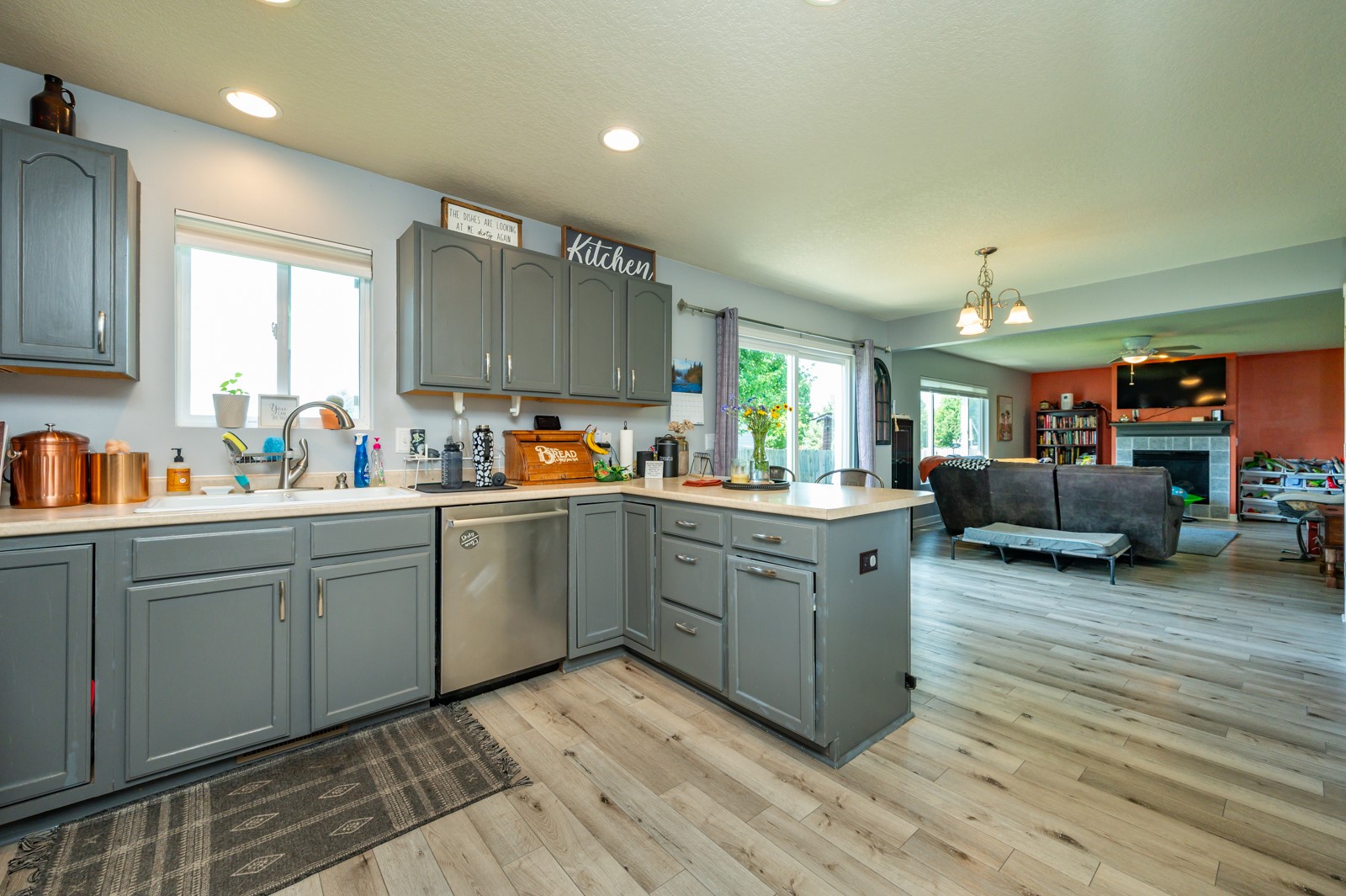 Kitchen with gray cabinets and a large island opening into a living room with a fireplace.
