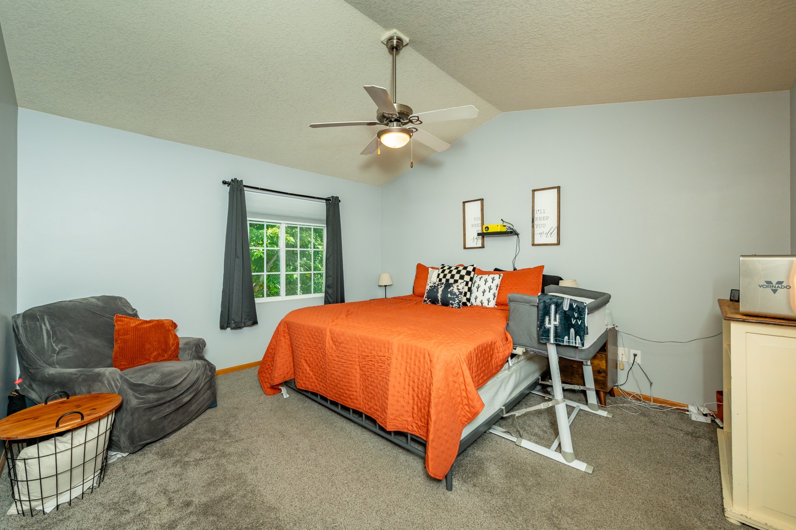 Bedroom with orange bedspread, gray chair, and a window framed by dark curtains.