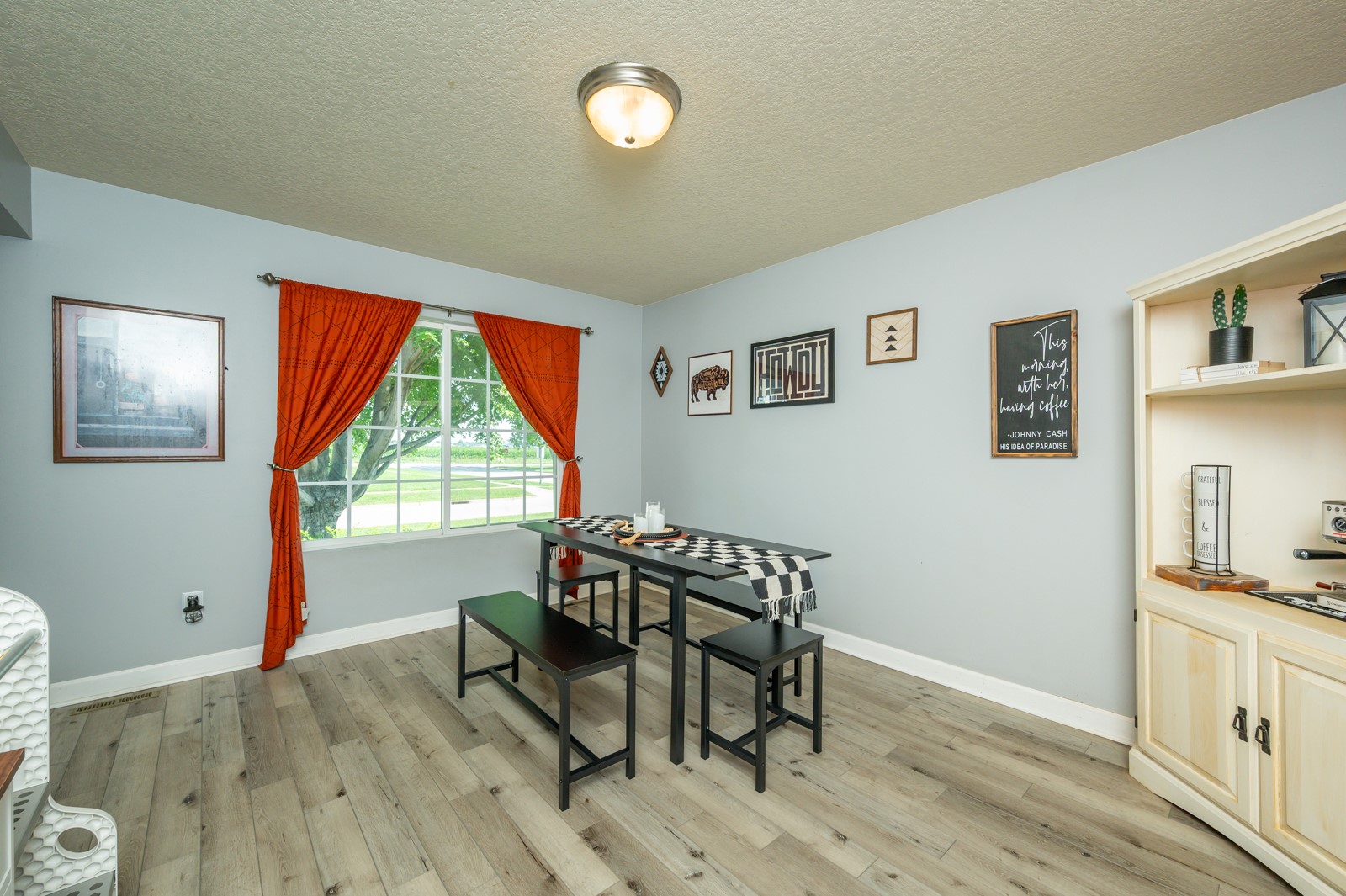 Dining room with a black table, checkered runner, orange curtains, and built-in cream cabinet.