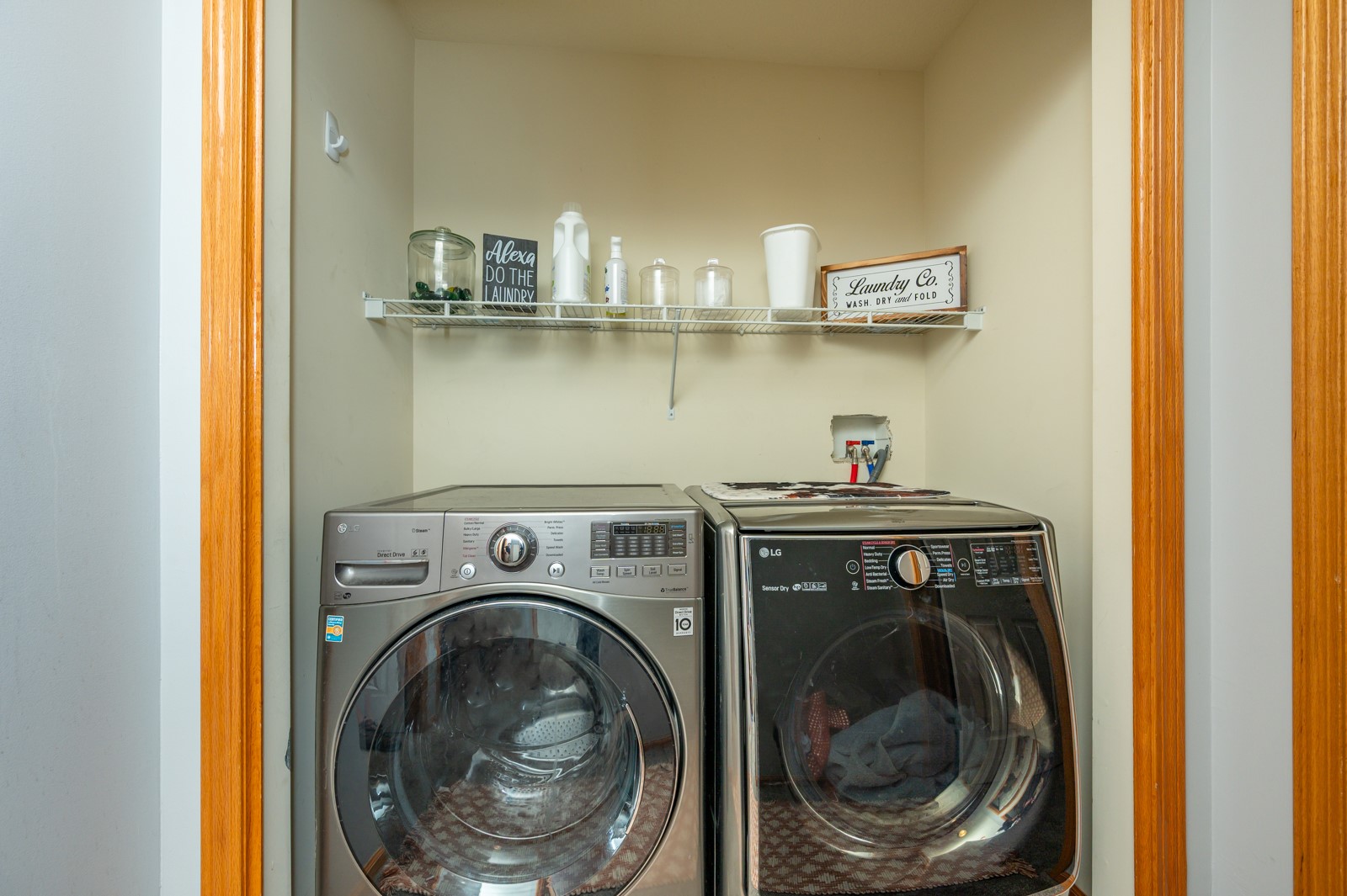 Laundry room with front-loading washer and dryer beneath a shelf of supplies.
