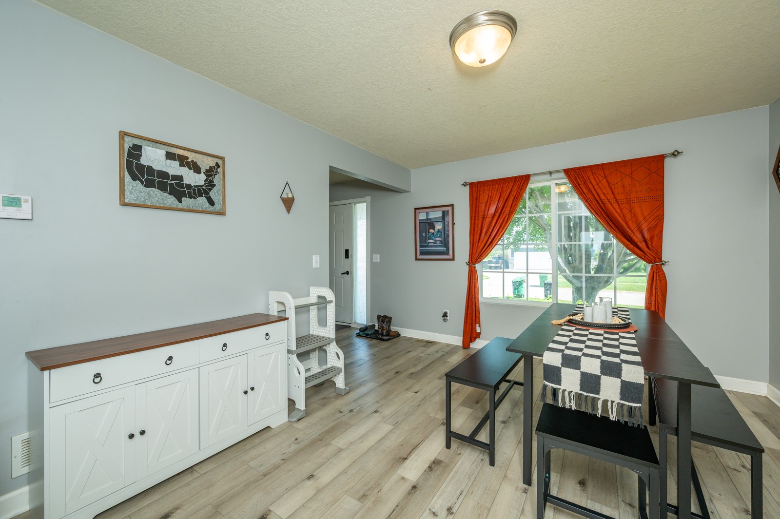 Dining area with a dark table, orange curtains, and a large street-facing window.