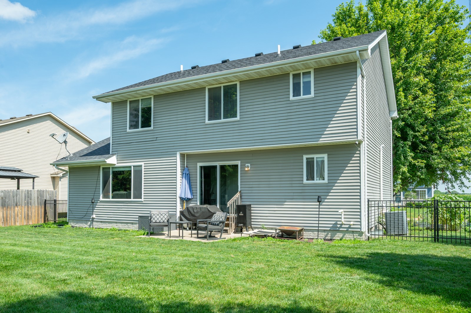 Rear of a two-story gray house with patio seating and a broad lawn.