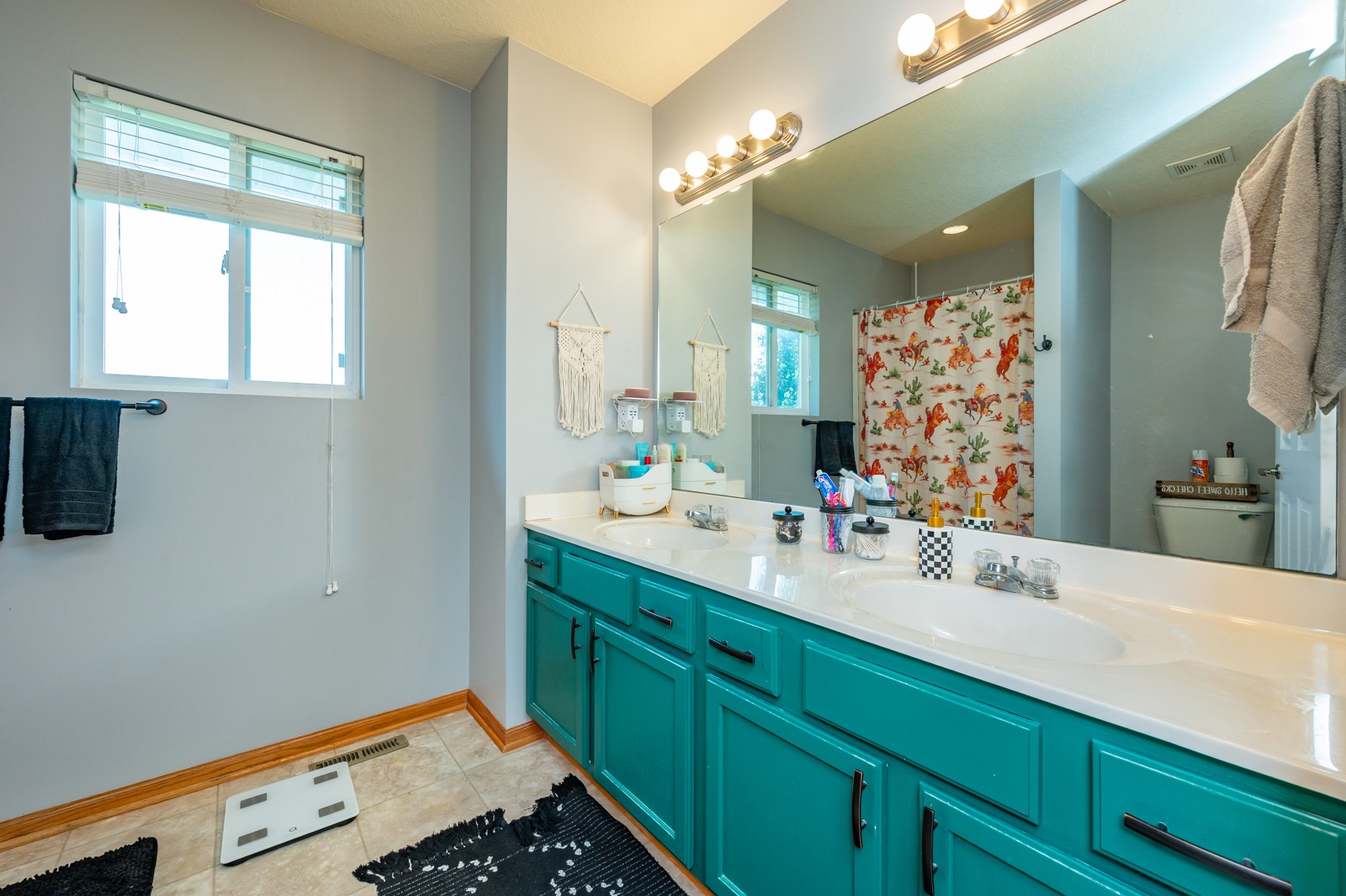 Bathroom with a turquoise double vanity, large mirror, and colorful Western-patterned shower curtain.