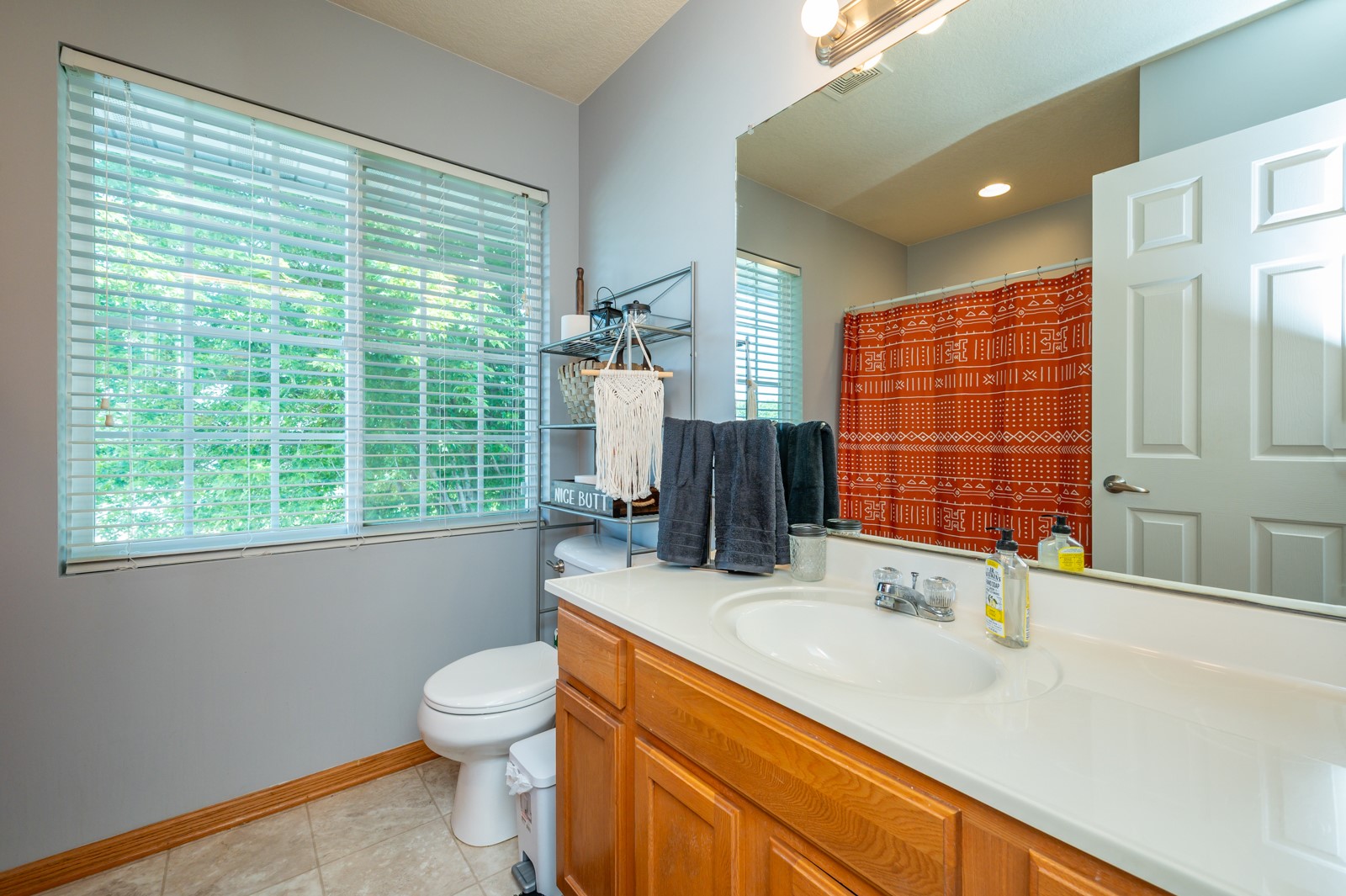 Bathroom with a wood vanity, large window, and red patterned shower curtain.