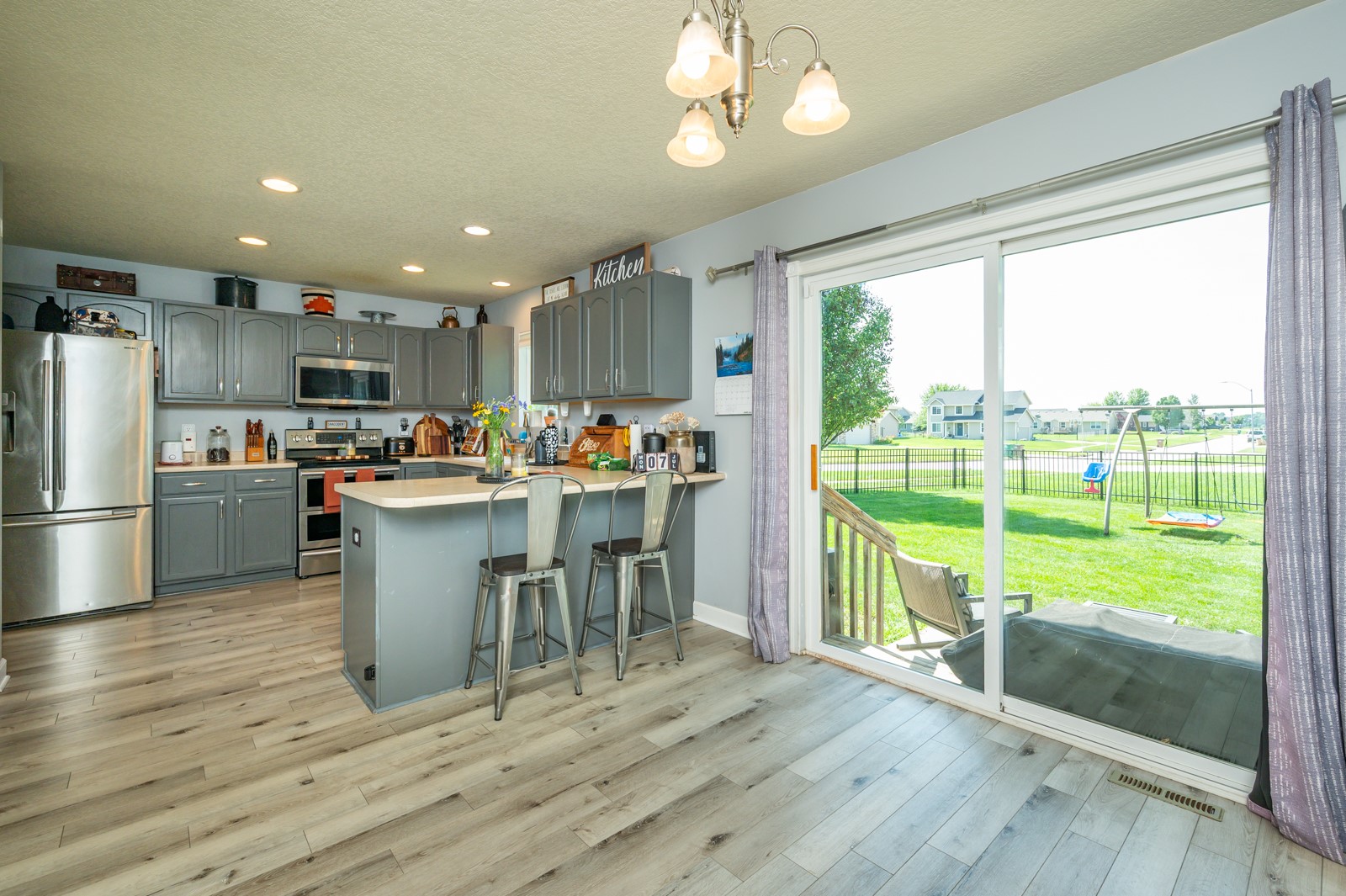 Kitchen with gray cabinetry and island, opening through sliding glass doors to a sunny backyard.