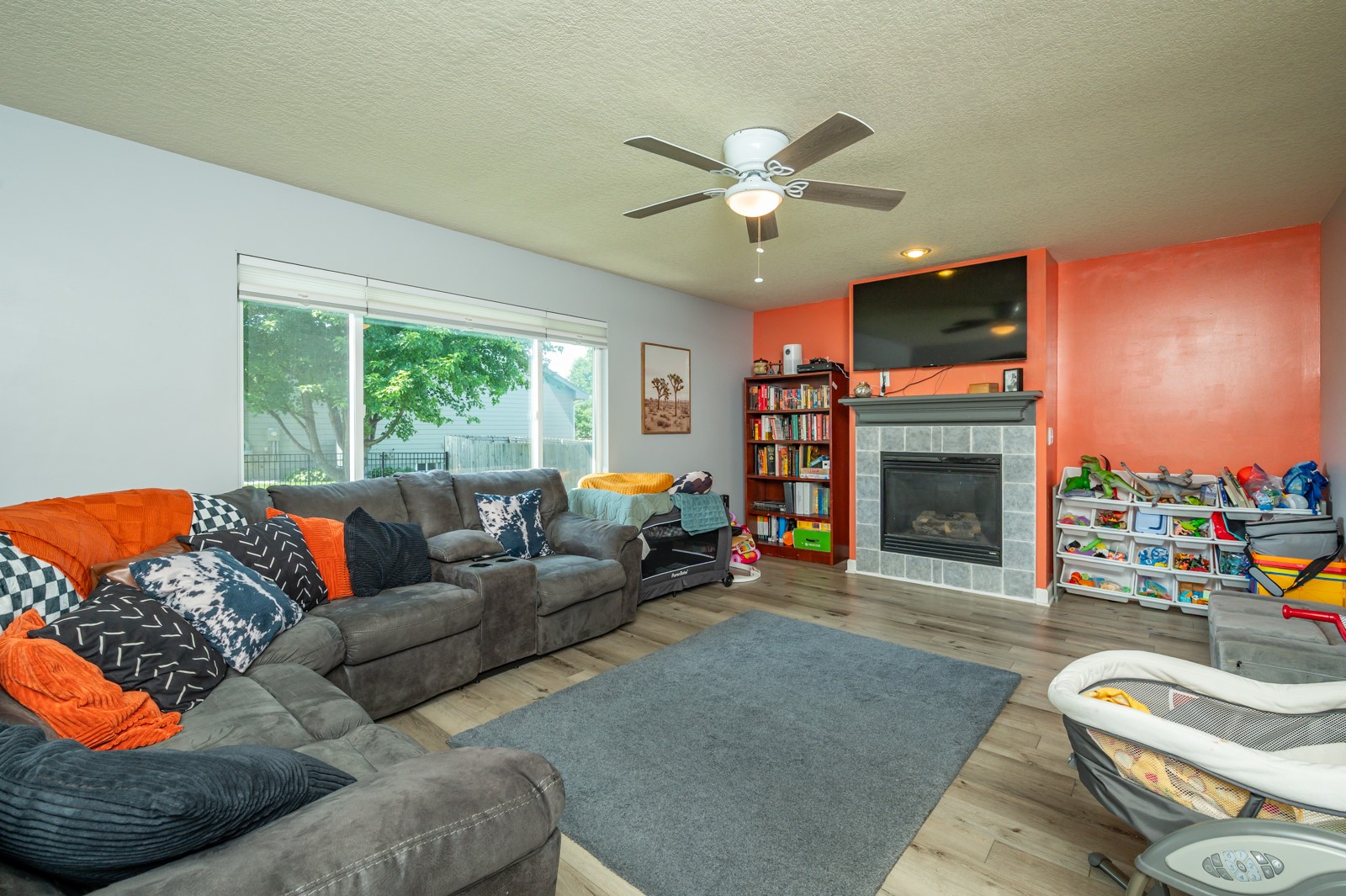 Living room with a gray sectional, sliding glass doors, tiled fireplace, and children’s toys.