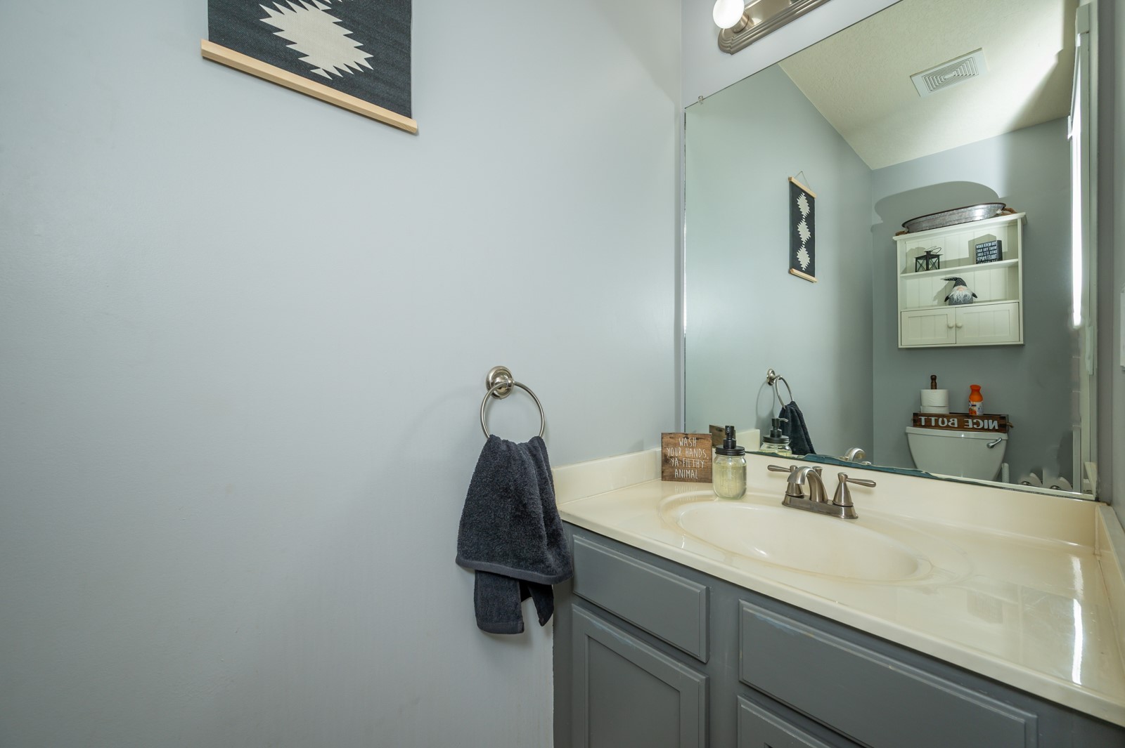 Bathroom vanity with an oval sink, large mirror, gray cabinets, and dark hand towel.