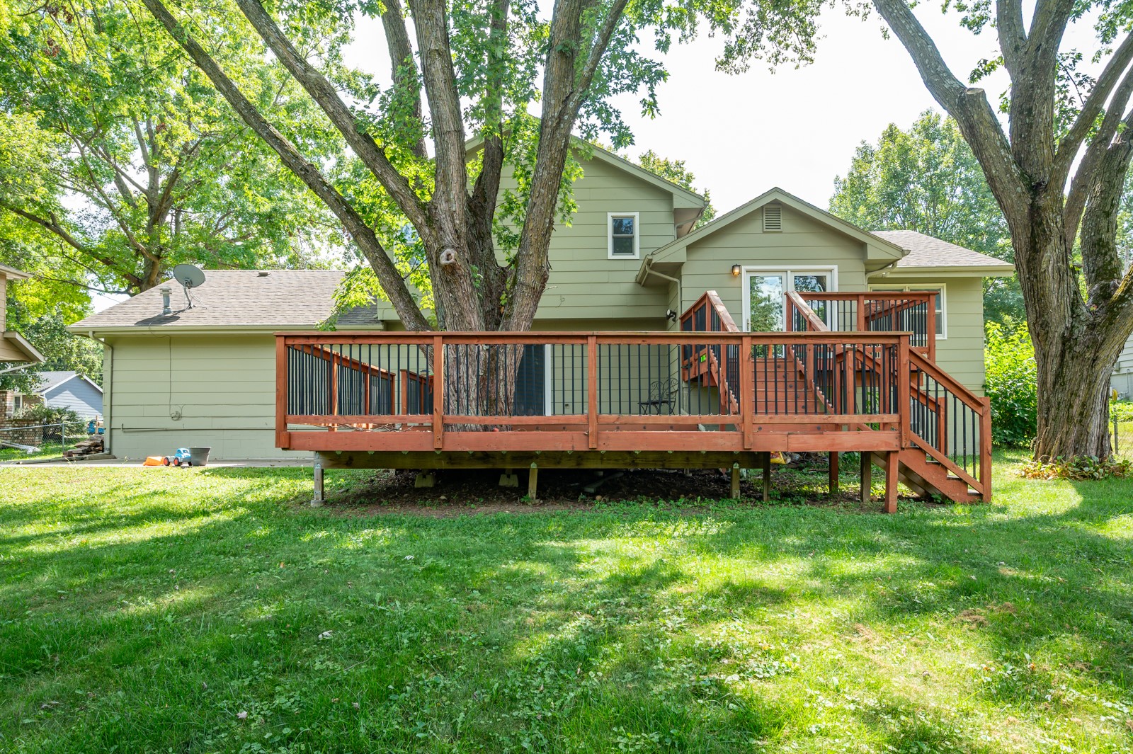 House rear with a raised wooden deck and stairs beneath mature trees.
