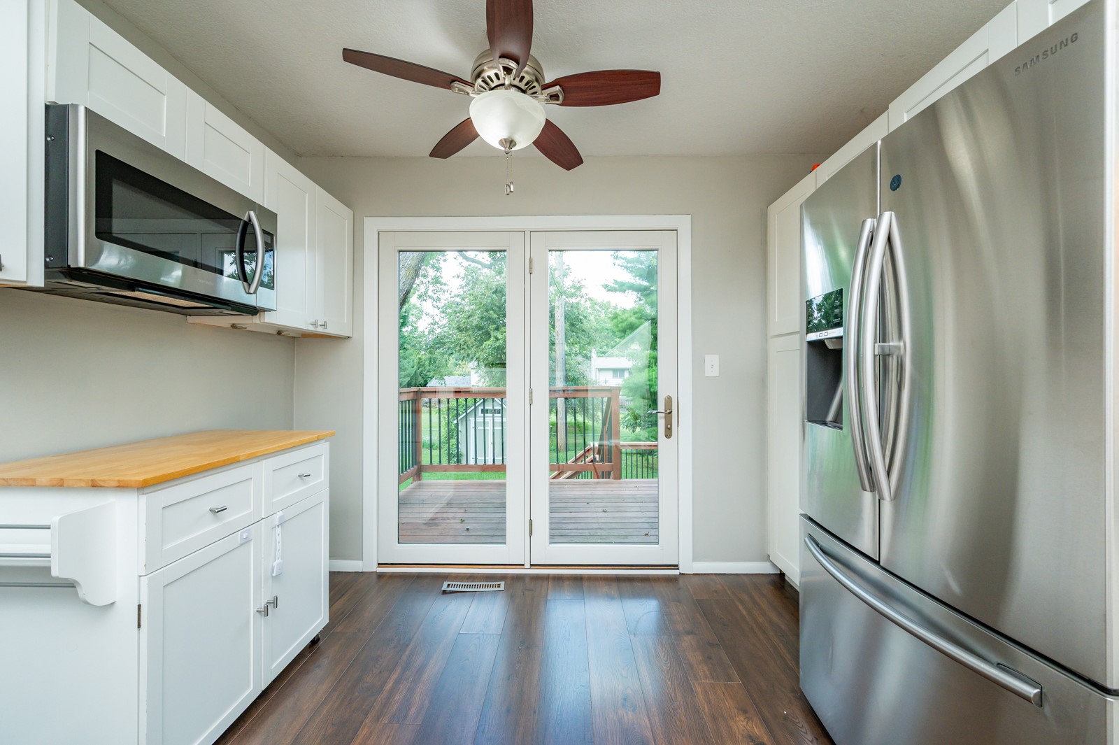 Kitchen with white cabinets and stainless appliances, opening through glass doors to a wooden deck.