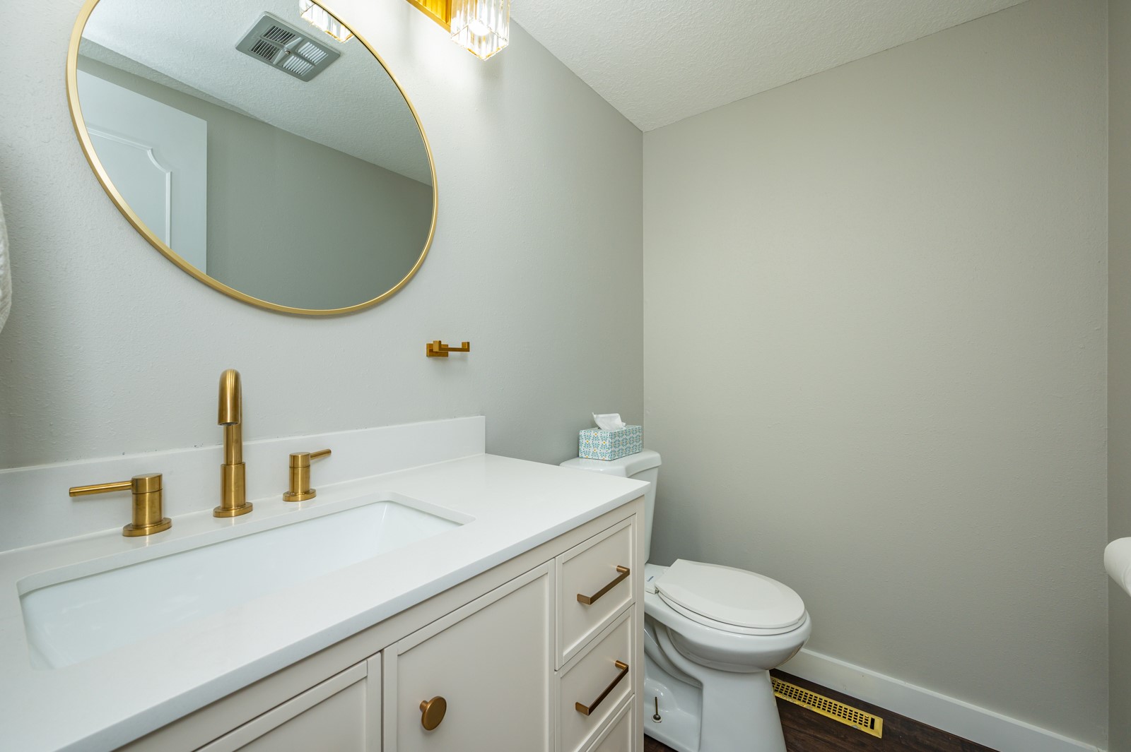 Bathroom with a white vanity, gold fixtures, oval mirror, and toilet.