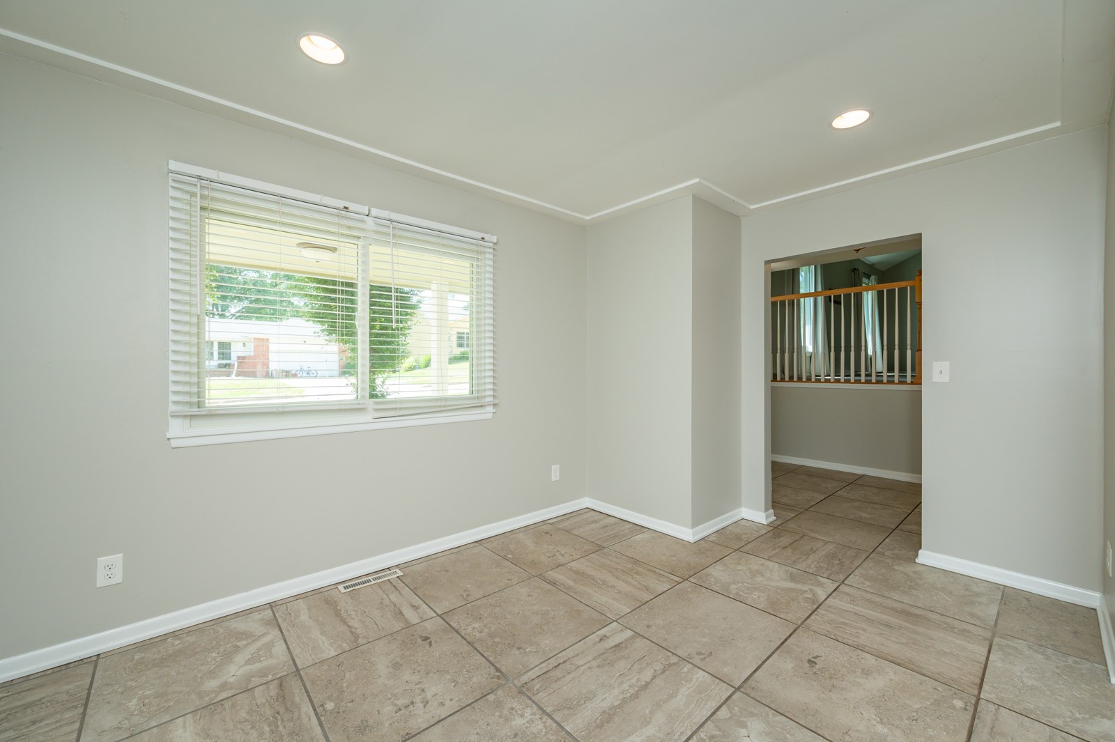 Empty tiled room with a wide window and an opening to a hallway with a railing.