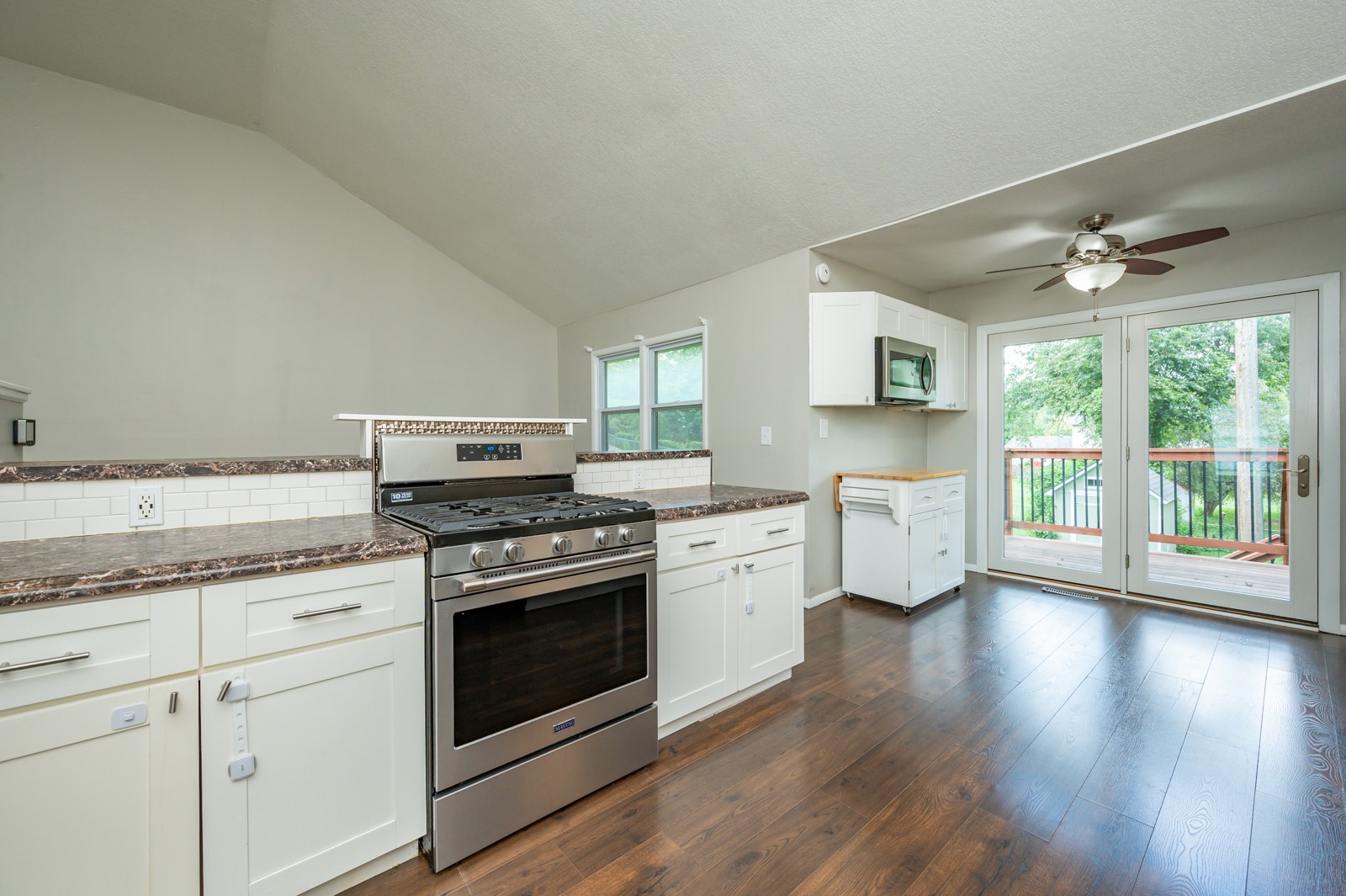 Kitchen with white cabinets, stainless steel gas range, and glass doors opening to a tree-lined deck.