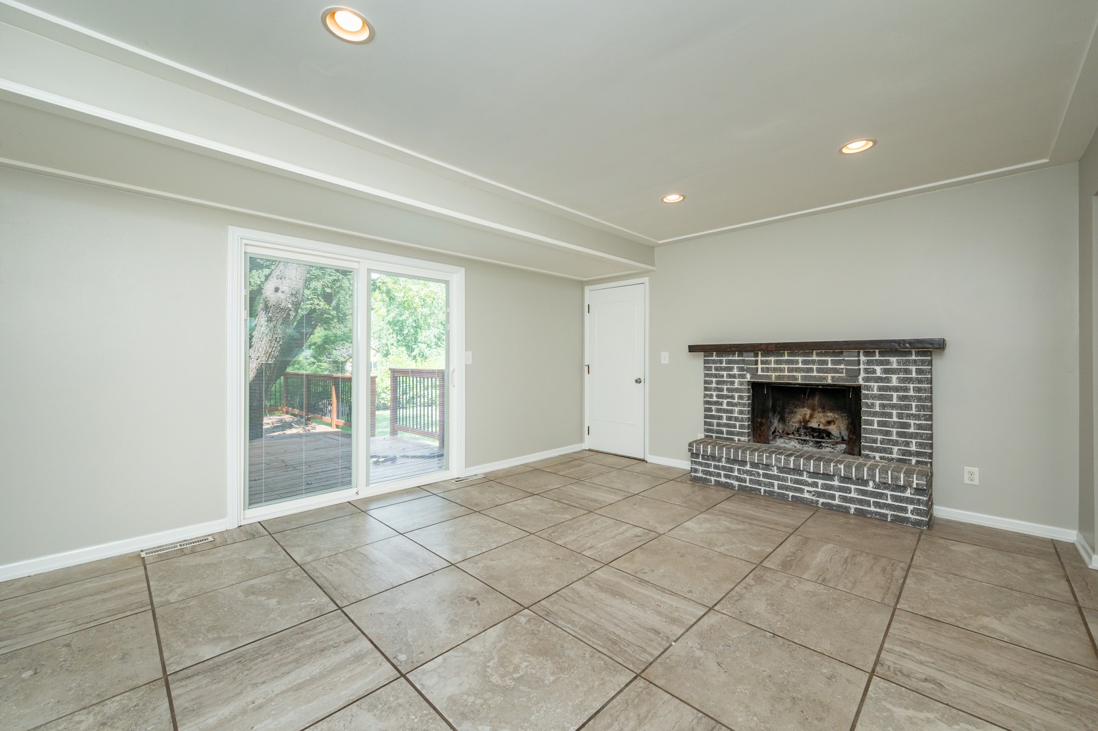 Empty living room with a brick fireplace, tiled floor, and sliding doors to a deck.