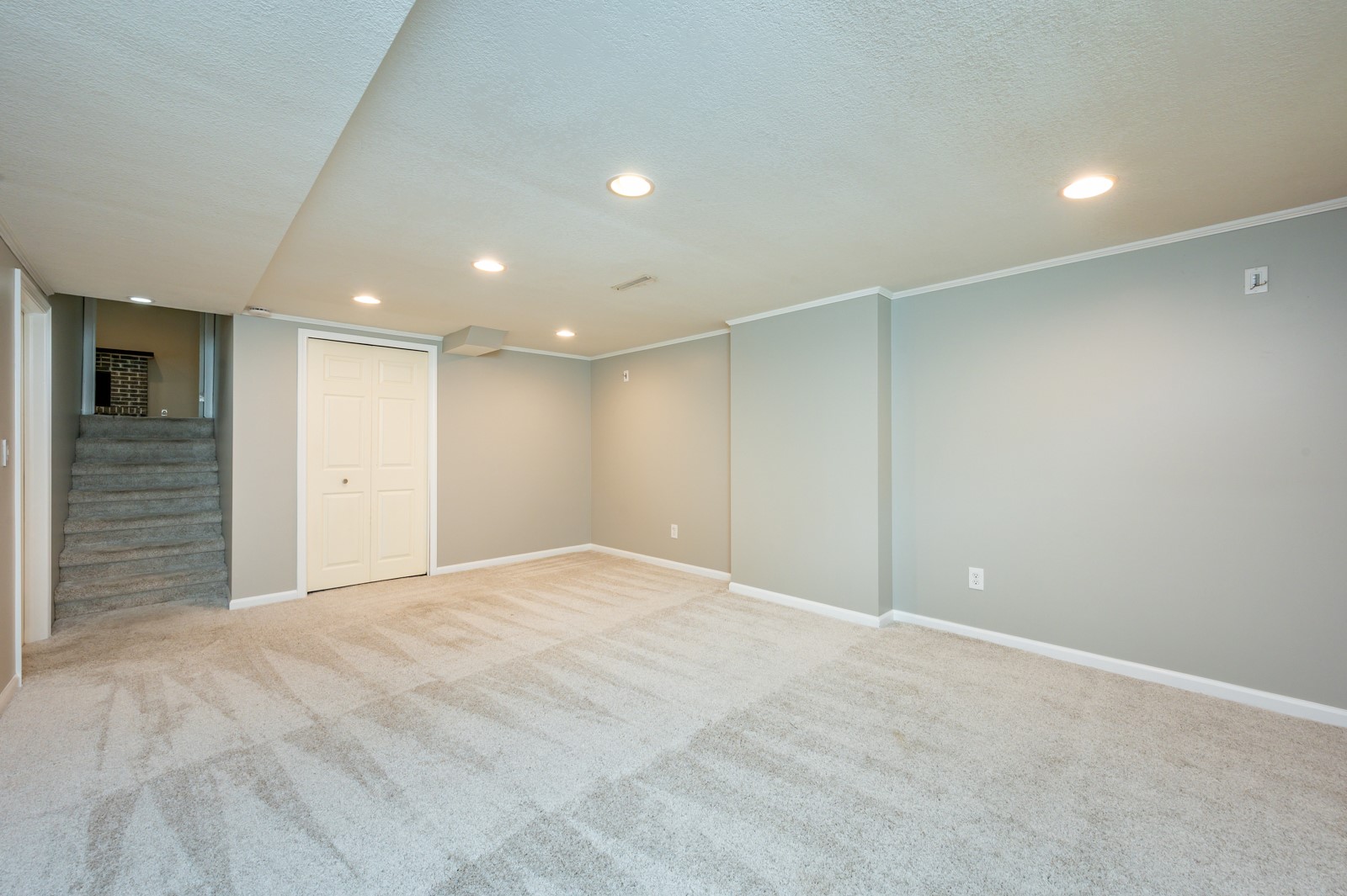 Finished basement room with light carpeting, recessed lights, and stairs.