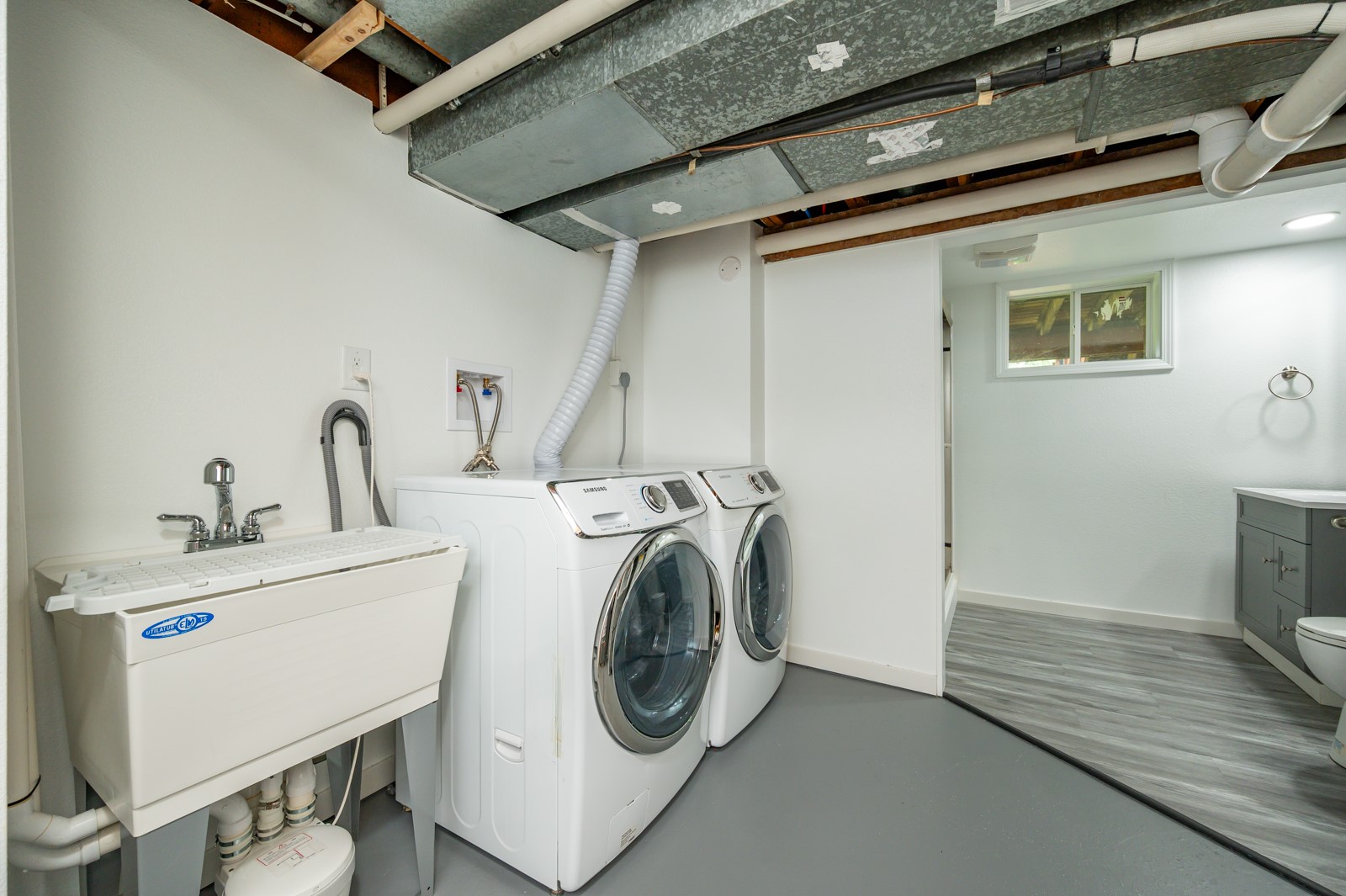 Basement laundry room with a utility sink, front-loading washer and dryer, and exposed ceiling ductwork.