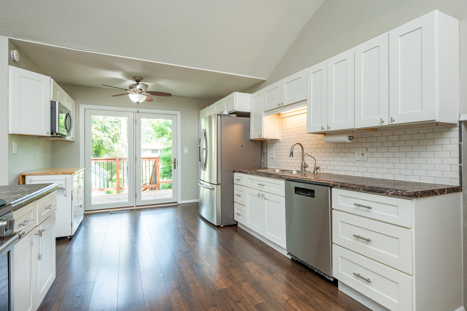 Kitchen with white cabinets, stainless steel appliances, dark wood floors, and glass doors to a deck.