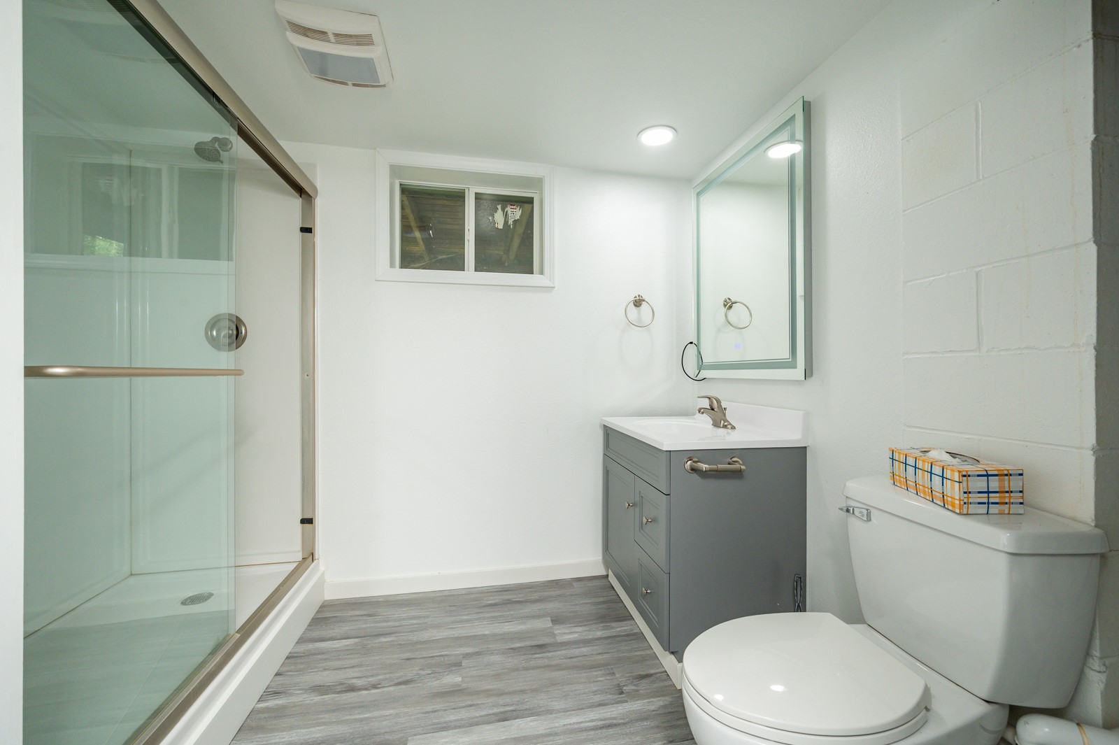 Bathroom with glass shower, gray vanity, mirrored cabinet, and gray wood-look floor.