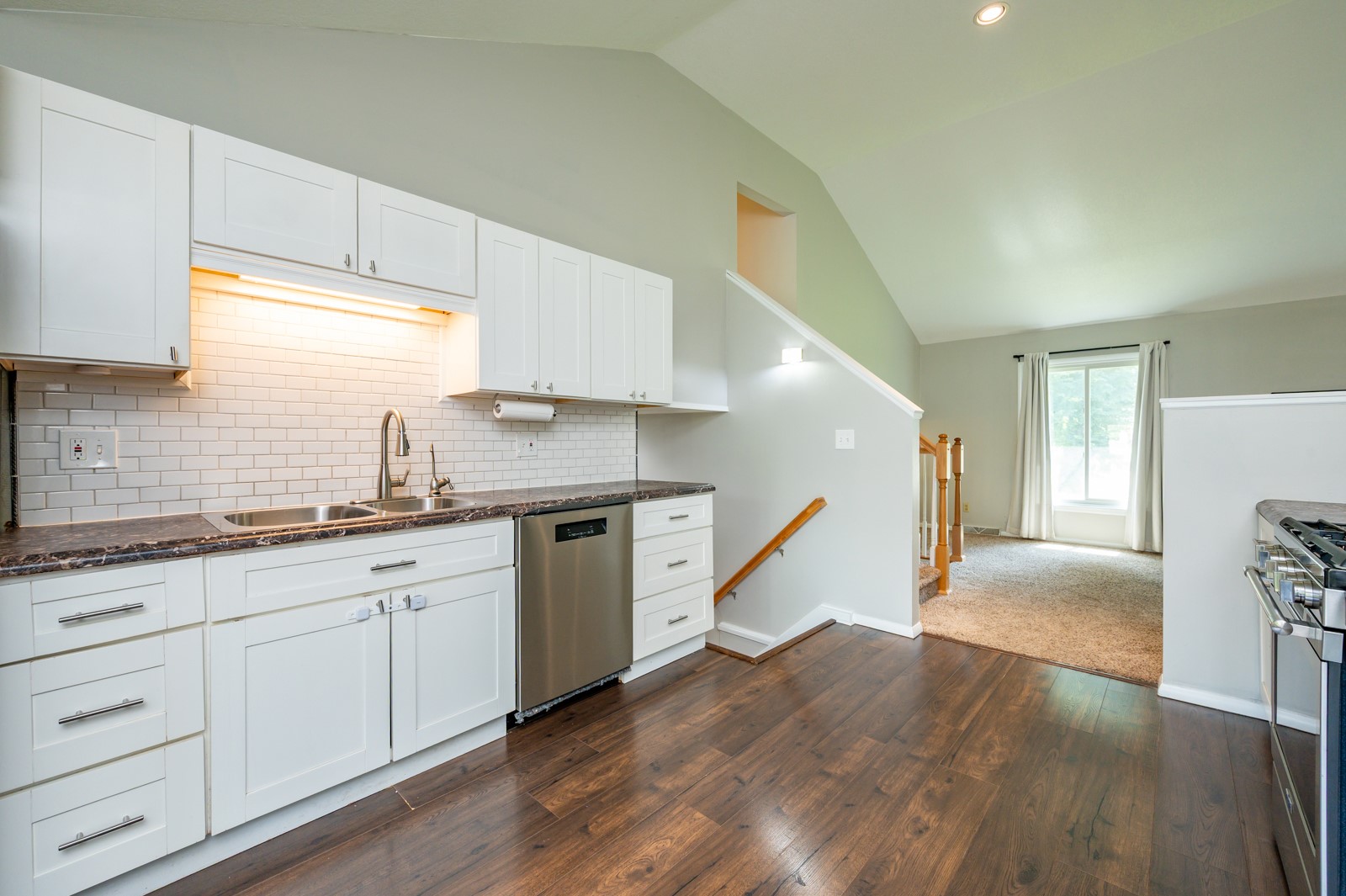 Kitchen with white cabinets, subway-tile backsplash, stainless steel appliances, and dark wood floors.
