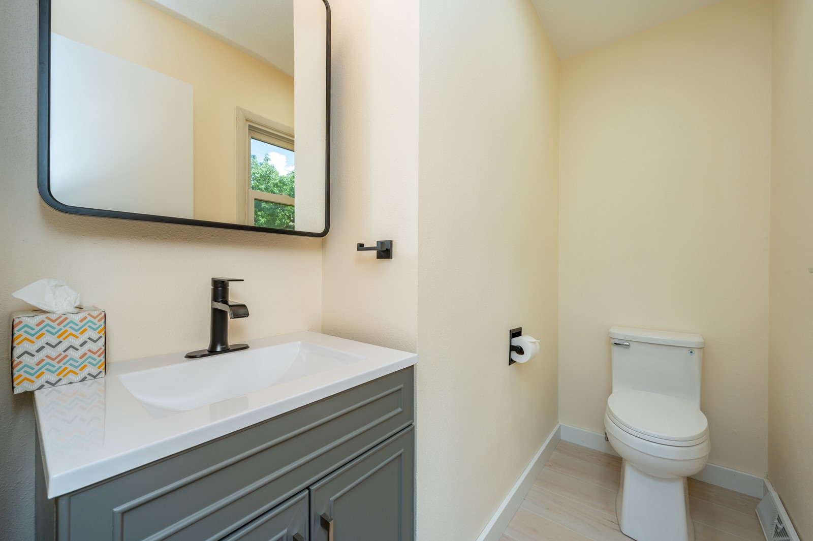 Bathroom with gray vanity, black fixtures, large mirror, and white toilet.