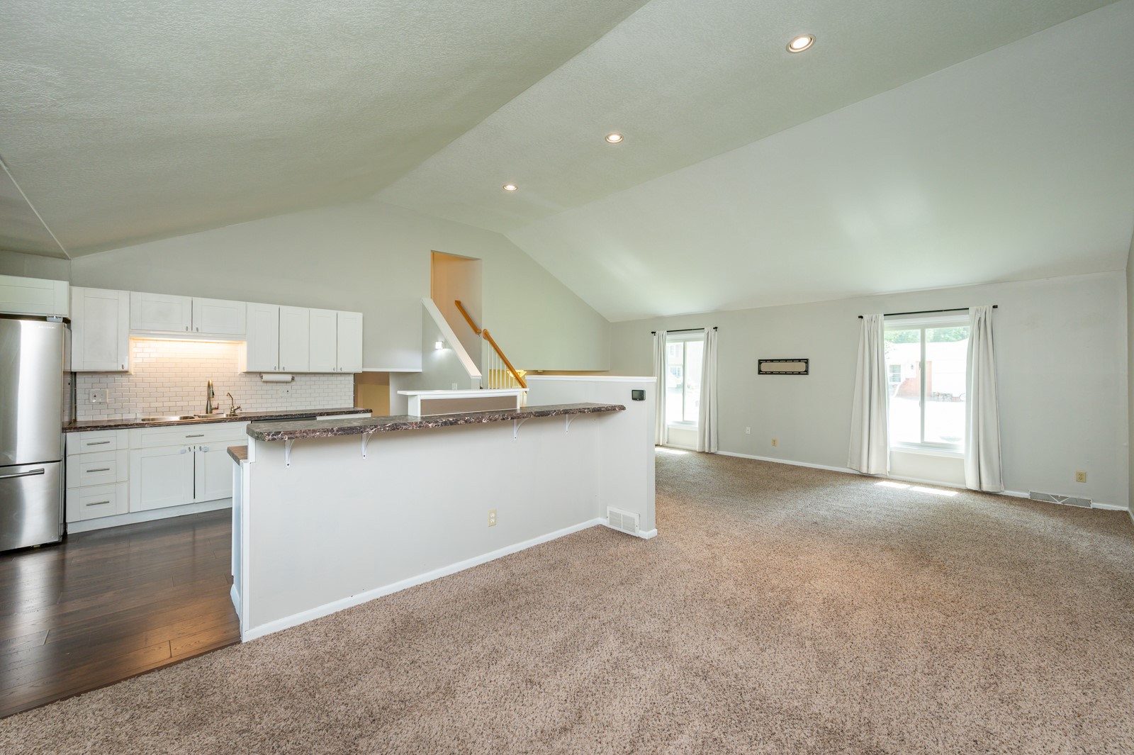 Open-plan kitchen and living area with white cabinetry, a breakfast bar, and vaulted ceiling.