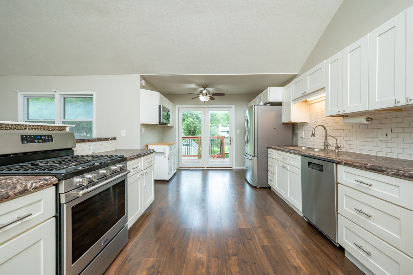 Kitchen with white cabinets, stainless steel appliances, dark wood floors, and glass doors to a deck.