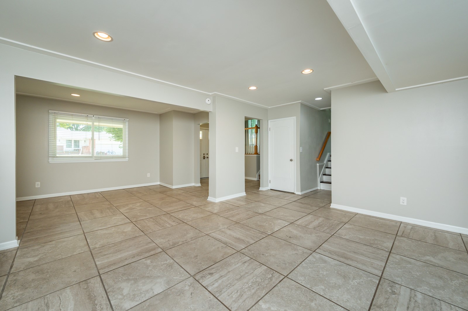 Empty living area with large beige tile floors and a staircase.