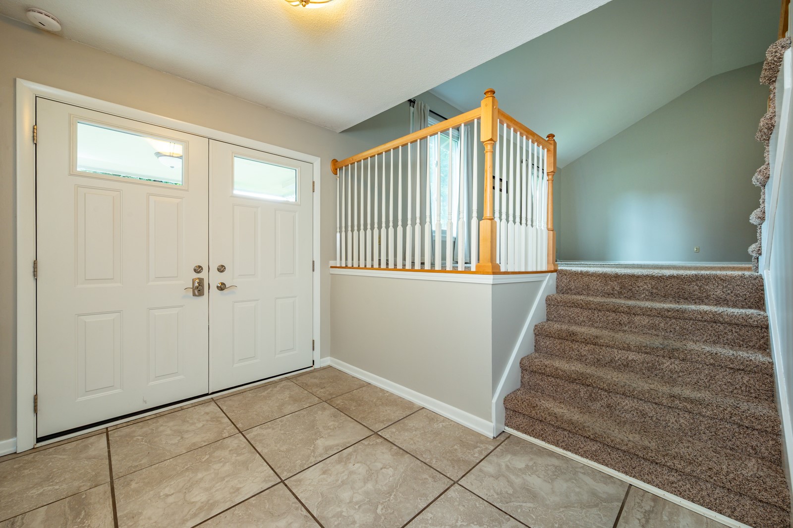 Entryway with tiled floor, double doors, and carpeted stairs with a wood-and-white railing.