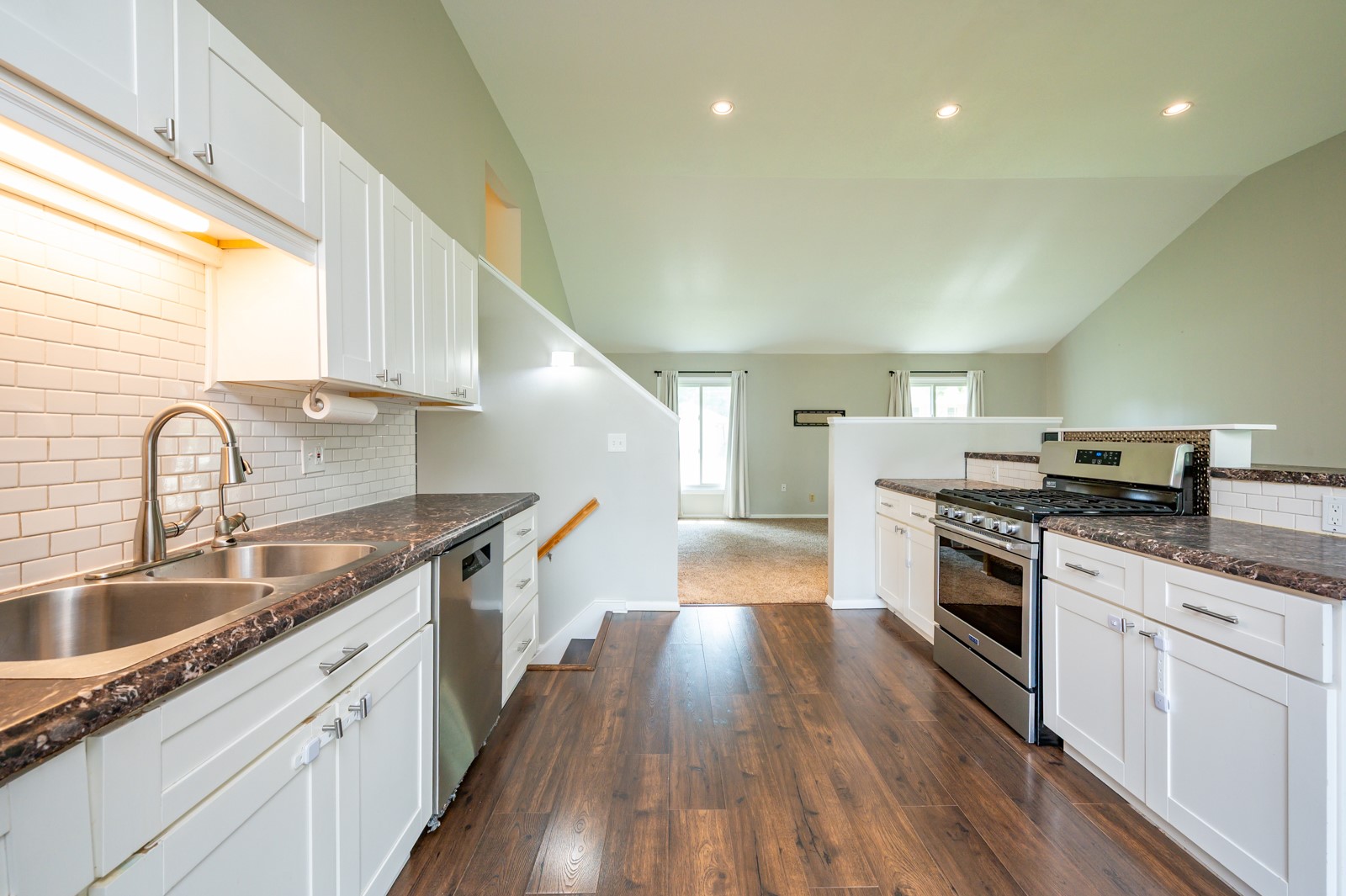 Kitchen with white cabinetry, dark countertops, subway tile backsplash, and stainless steel range opening to a living area.