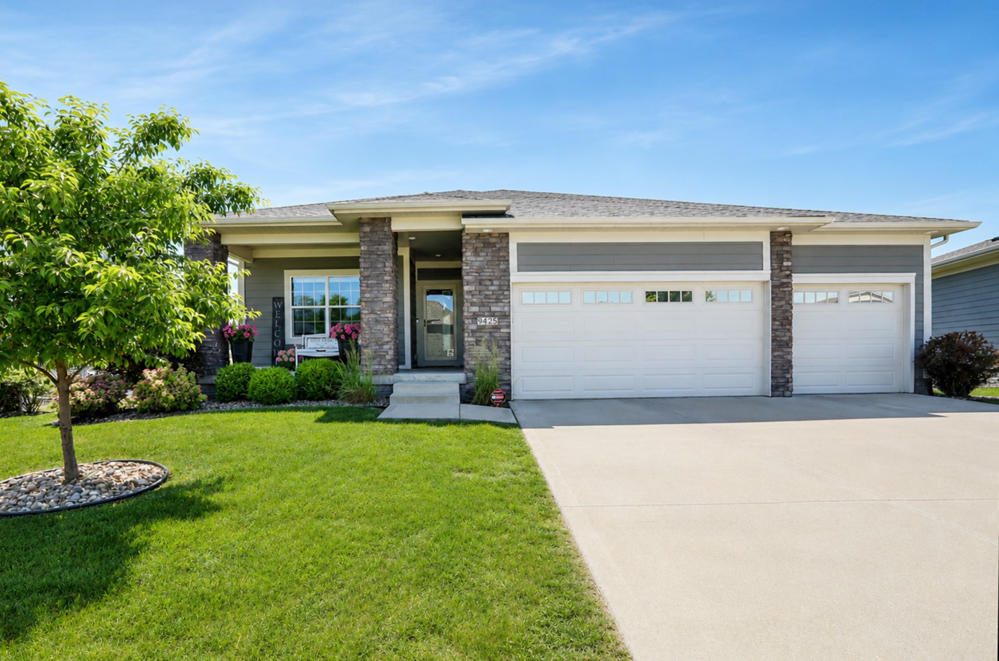 Gray single-story home with stone columns, three-car garage, and landscaped front lawn.
