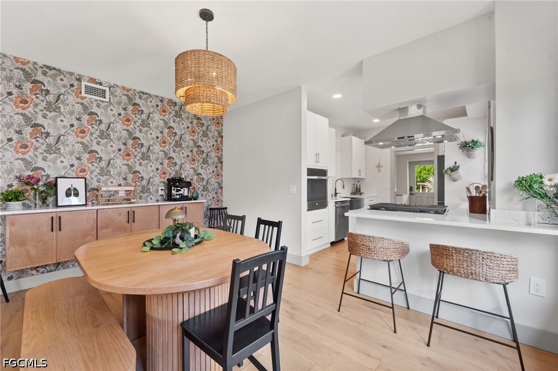 Open-plan kitchen and dining area with a large island, woven stools, and floral wallpaper.