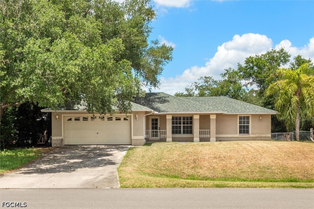 Single-story beige house with an attached two-car garage, driveway, and mature trees.