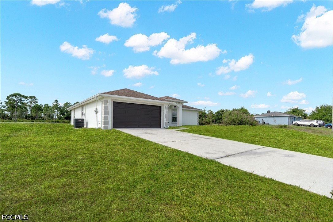 Single-story white house with a dark double garage door, long concrete driveway, and broad grassy yard.