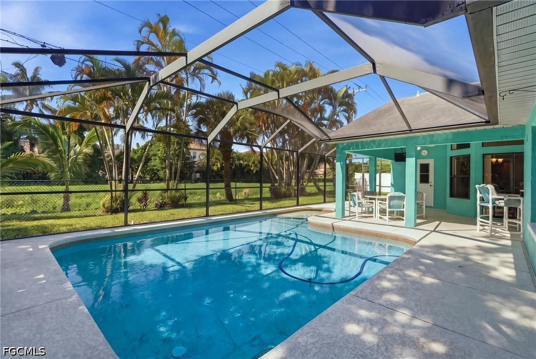 Swimming pool in a screened lanai beside a turquoise patio with white outdoor dining furniture.