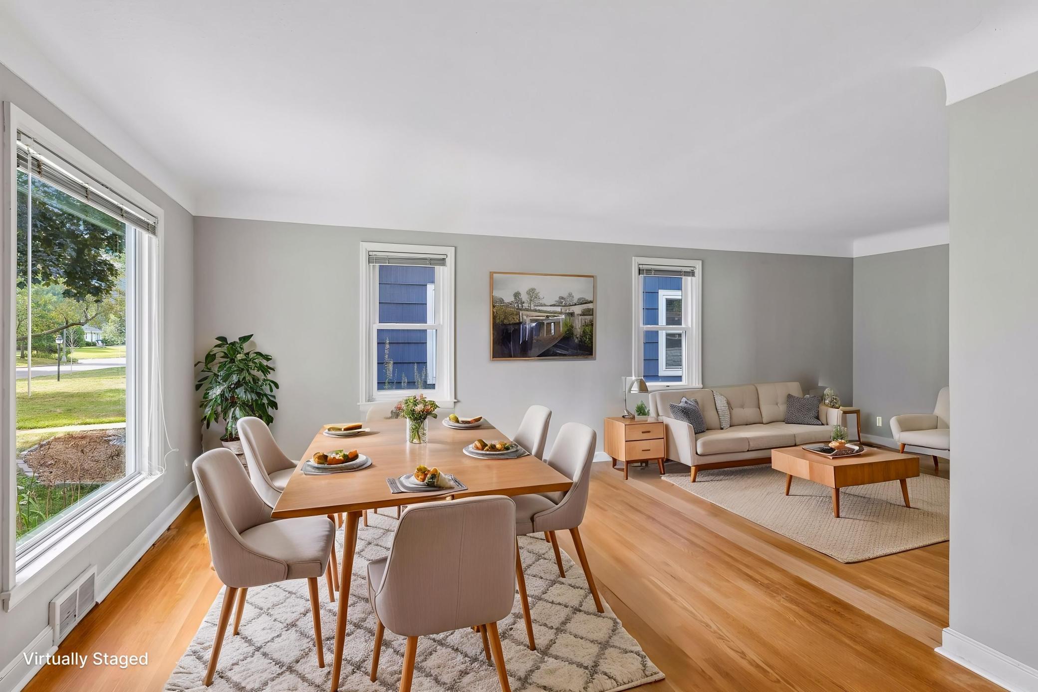 Open-plan dining and living room with a wood table, beige sofa, and large windows.