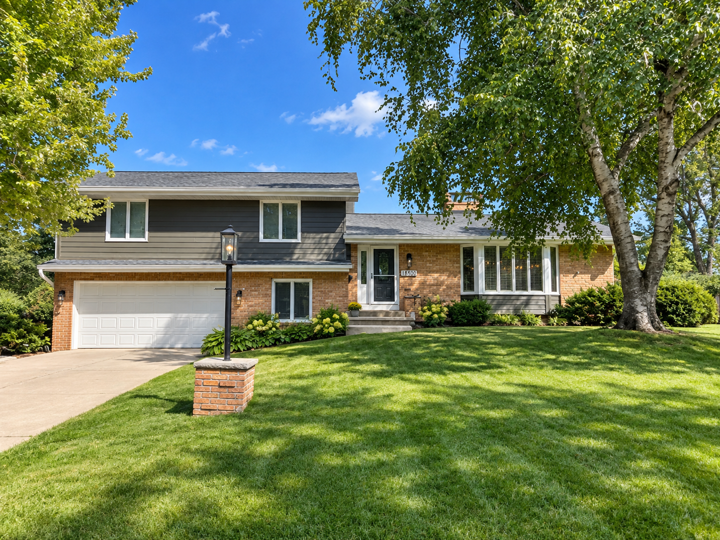Two-story brick and gray-sided home with an attached garage, broad lawn, and mature trees.