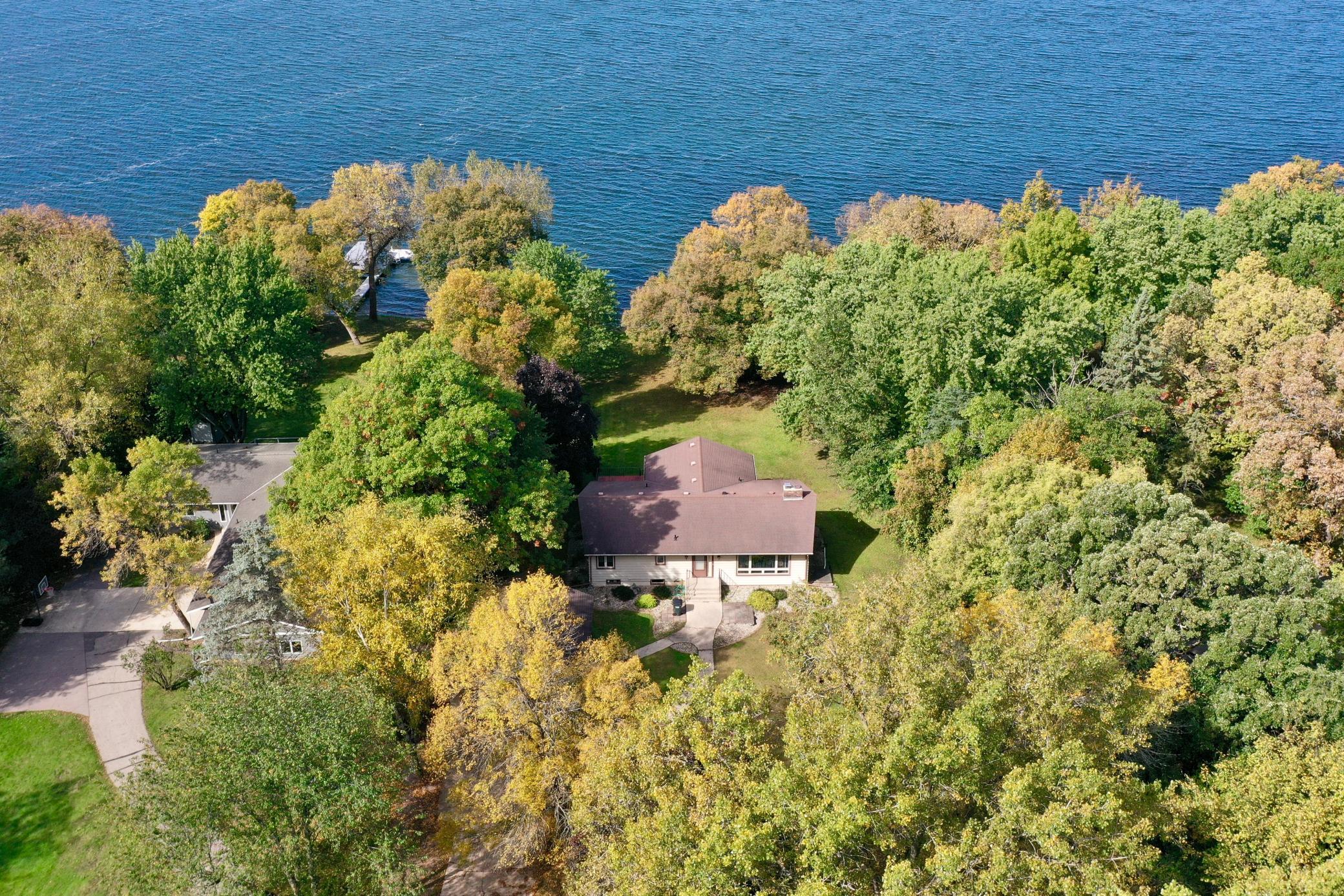 Aerial view of a lakeside home surrounded by autumn trees and lawn.