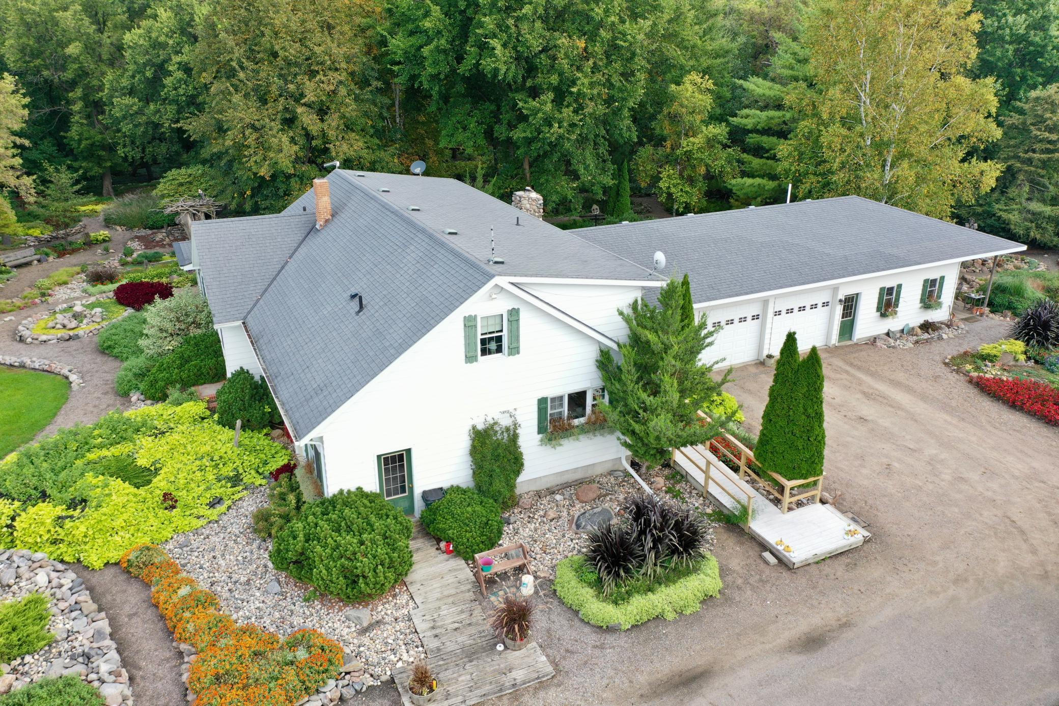 Aerial view of a white home with a broad gray roof, attached garages, and landscaped grounds.