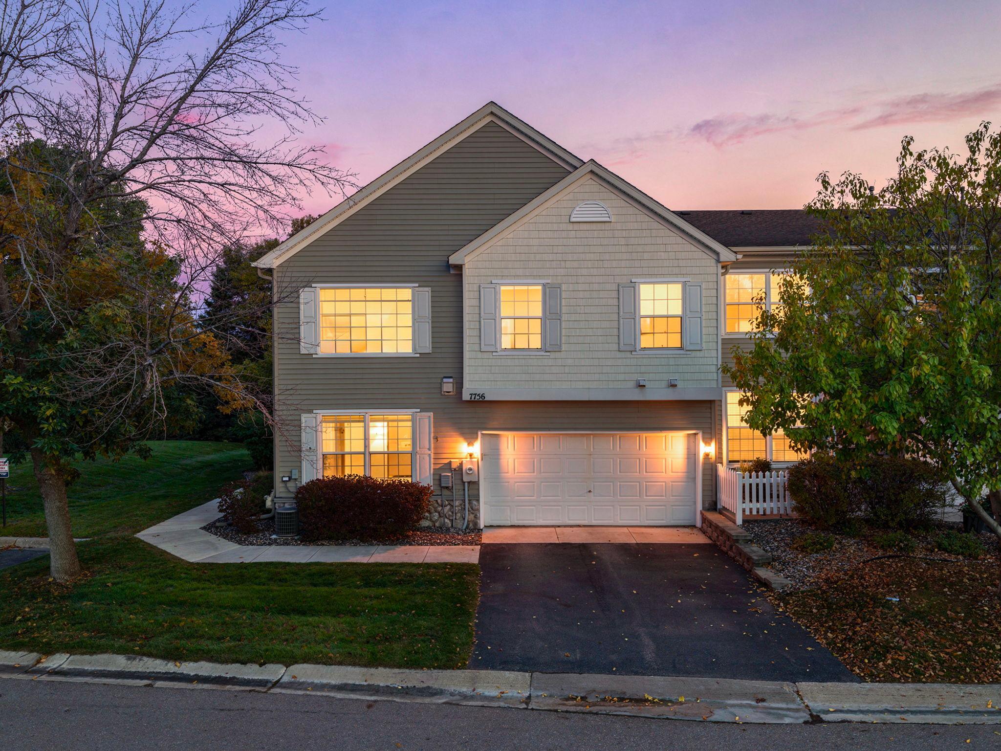Two-story house with a garage and warmly lit windows at dusk.