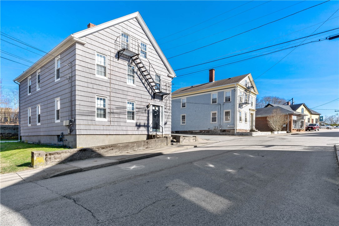 Gray multi-story shingle-sided building with black metal fire escapes beside a residential street.