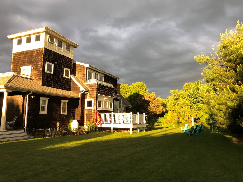 Shingle-clad home with a tower, white-railed deck, and lawn in warm evening light.