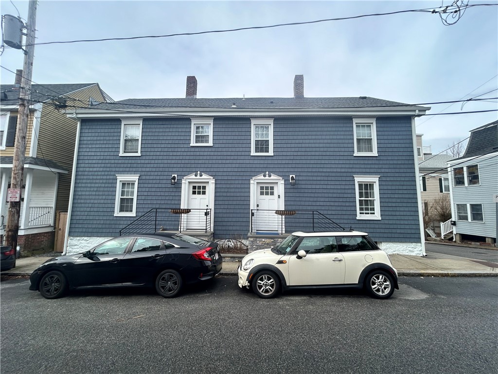 Blue-shingled two-story home with two front entrances and cars parked at the curb.