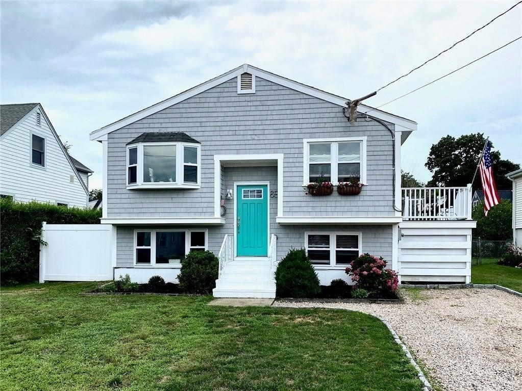Gray-shingled raised ranch with a turquoise front door, bay window, and American flag.